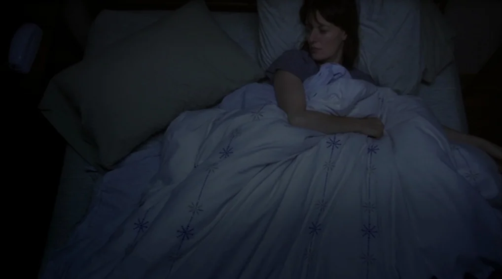 Your Sister’s Sister (2011) movie still: medium — A dark bedroom shows a woman lying in a bed under a patterned quilt. The woman is resting with her…