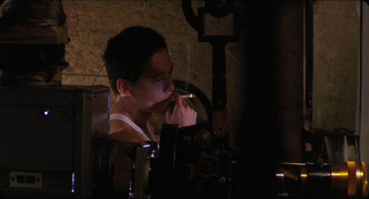 Goodbye, Dragon Inn (2003) movie still: medium — A dark projection booth contains mechanical film equipment and warm low light. A man in a white…