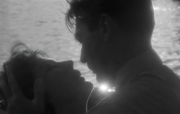 On The Beach (1959) movie still: closeup — Two individuals are positioned close together with water in the background. The couple moves toward one…