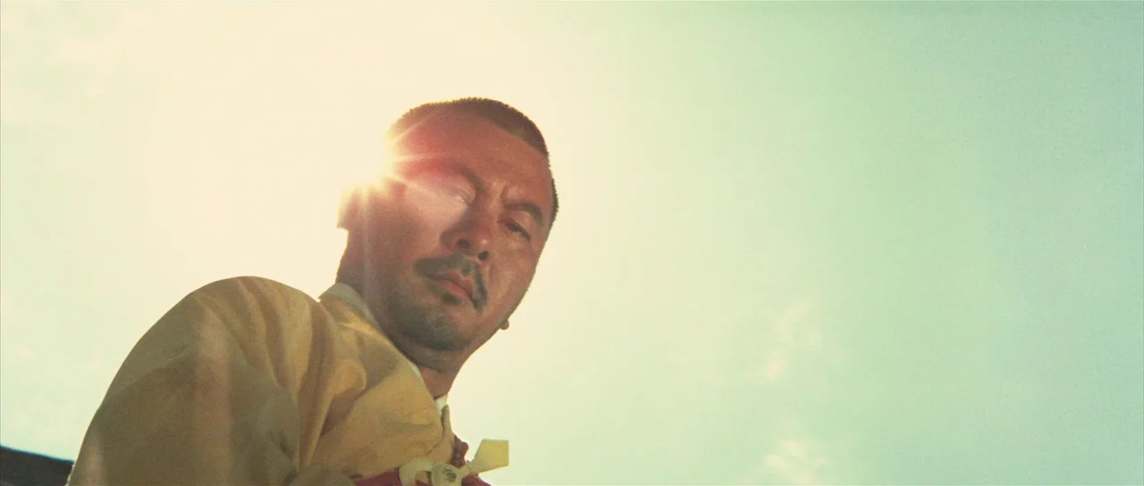 A Touch of Zen (1971) movie still: medium — An open area under a bright, cloudless sky. A man stands looking down at the camera against a…