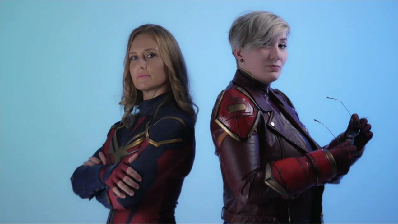 Reign of the Superwomen (2021) movie still: medium — A studio space with a flat, bright blue backdrop behind two standing women. The two women are…