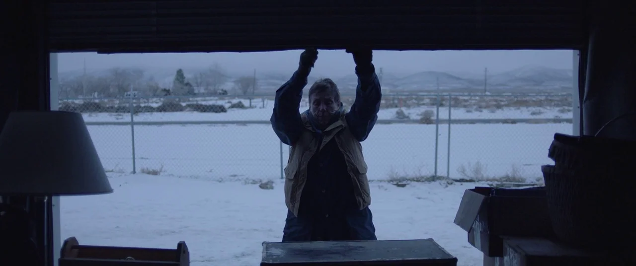 Nomadland (2020) movie still: medium — A dark, cluttered storage unit opens up to a vast, snowy, overcast landscape. An older man stands in the…