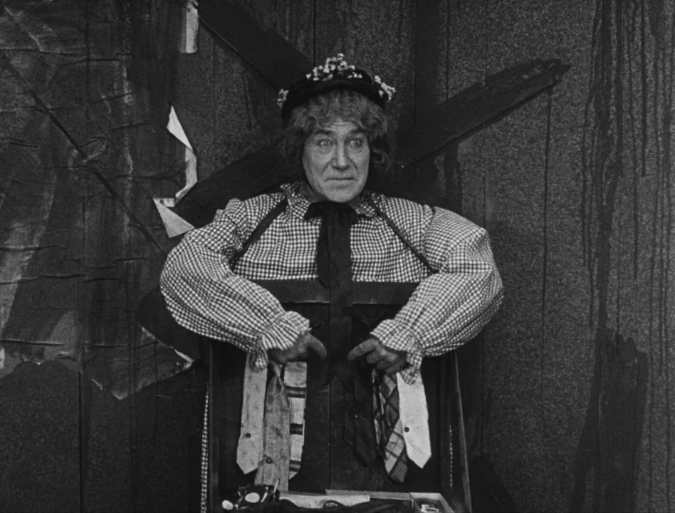 Sherlock Jr. (1924) movie still: medium — A man wearing a patterned shirt and hat poses in front of a backdrop. He leans over a small wooden…