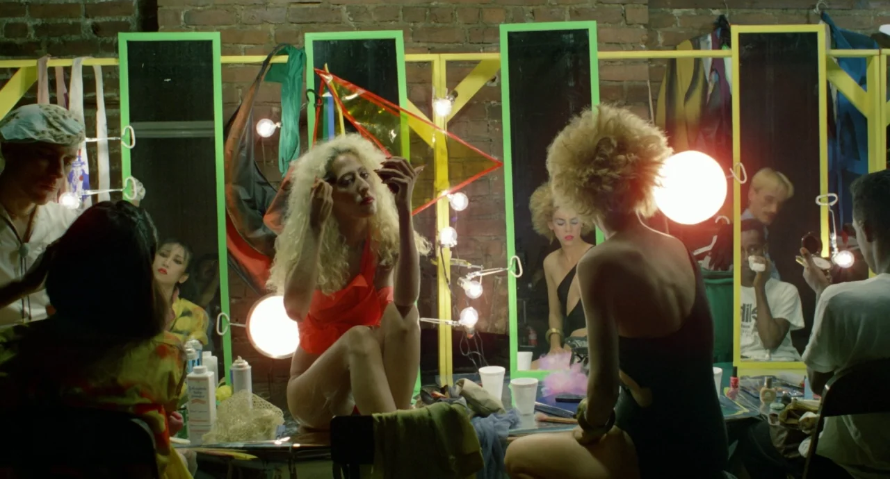 Liquid Sky (1982) movie still: medium — A cluttered backstage area features rows of mirrors framed in bright green and yellow. Several performers in…
