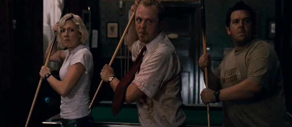 Shaun Of The Dead (2004) movie still: medium — Three people stand in a dimly lit, dark wood-paneled room. Each person holds a pool cue like a weapon…