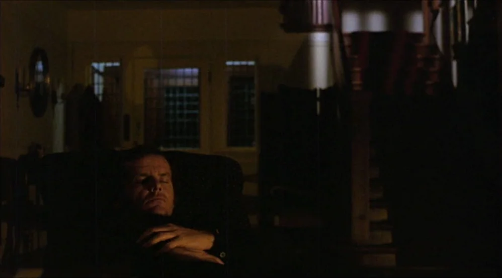 Five Easy Pieces (1970) movie still: medium — A dimly lit room with heavy shadows features a staircase in the background. A man sits alone in a dark…