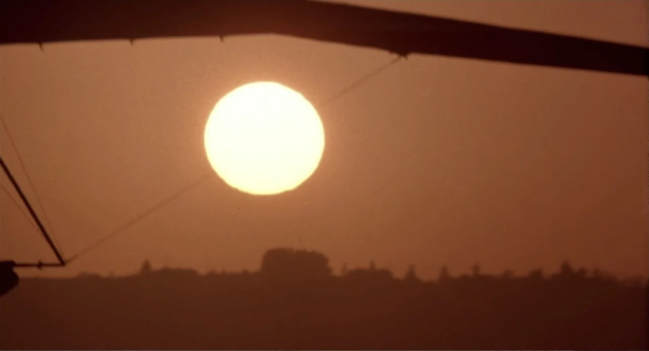 American Ninja 3: Blood Hunt (1989) movie still: establishing — A bright golden sun sits above a dark, silhouetted horizon line of distant trees.…