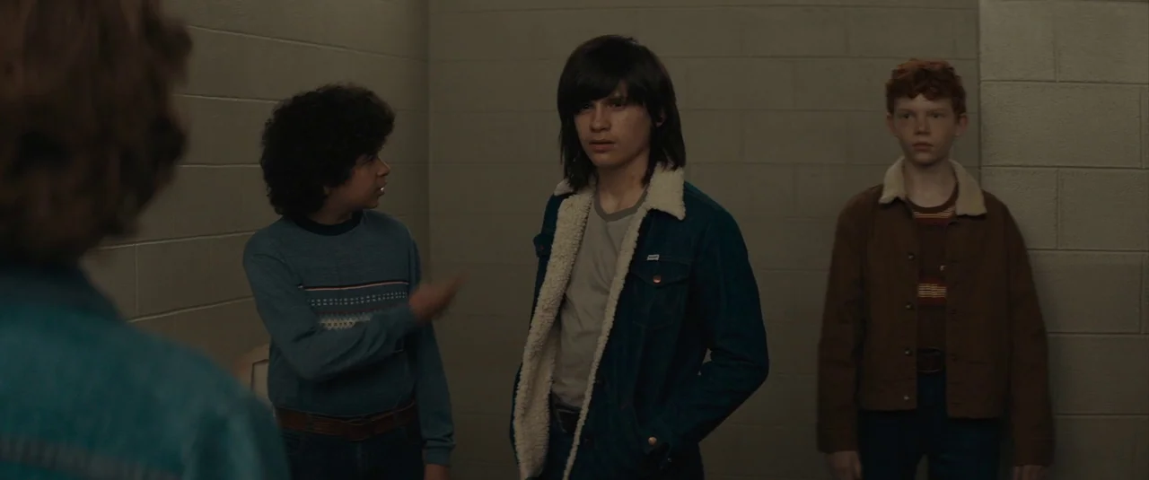 The Black Phone (2021) movie still: medium — An interior space with plain, light-colored concrete block walls in a muted environment. Three teenage…