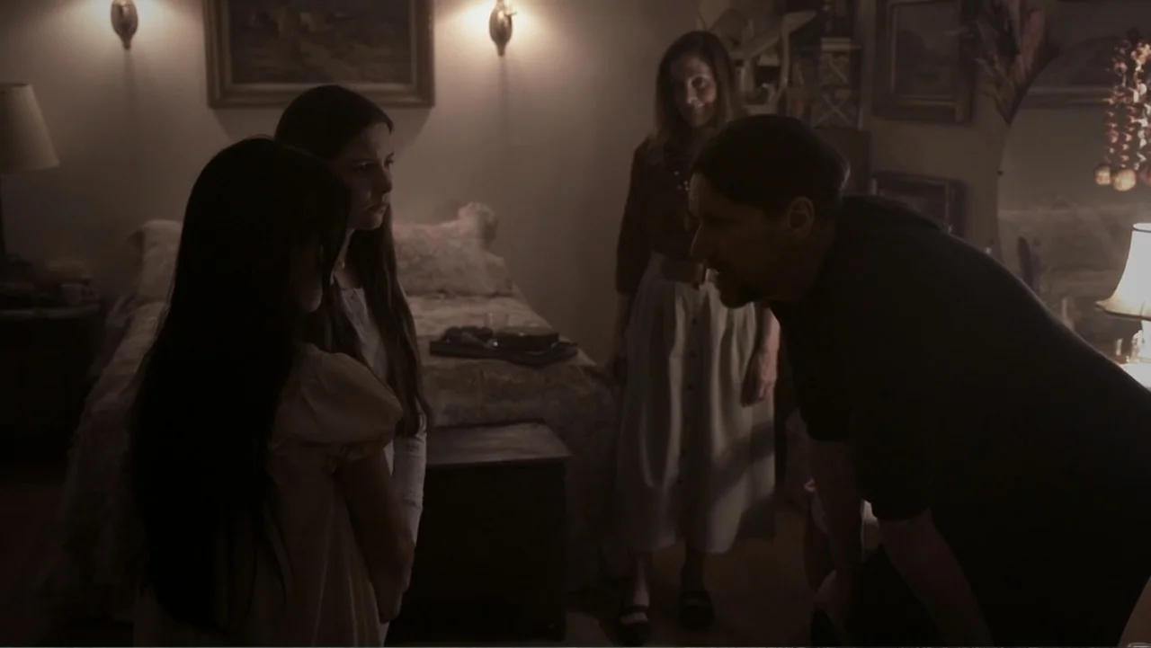 Paranormal Activity: The Ghost Dimension (2015) movie still: medium — A dimly lit bedroom features a bed with floral bedding and framed pictures. A…