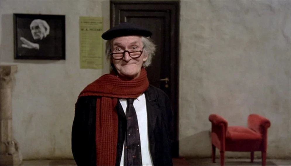 Orchestra Rehearsal (1978) movie still: medium — An interior space features textured beige walls with a small framed portrait and poster. A man in a…