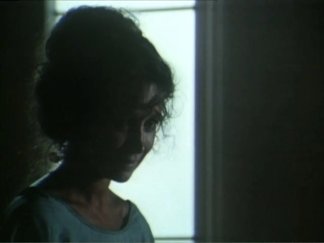 Curtains (1995) movie still: closeup — An indoor space features a woman standing near a window with visible window panes. She faces slightly away…