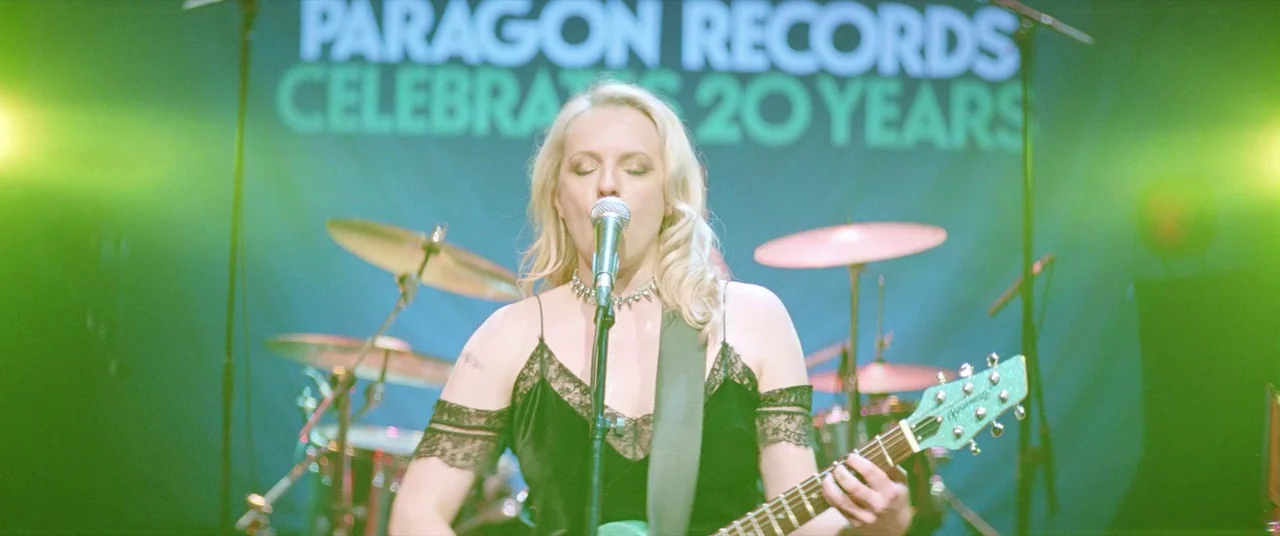 Her Smell (2018) movie still: medium — A woman performs on a stage in front of a branded record company banner. She sings with closed eyes while…