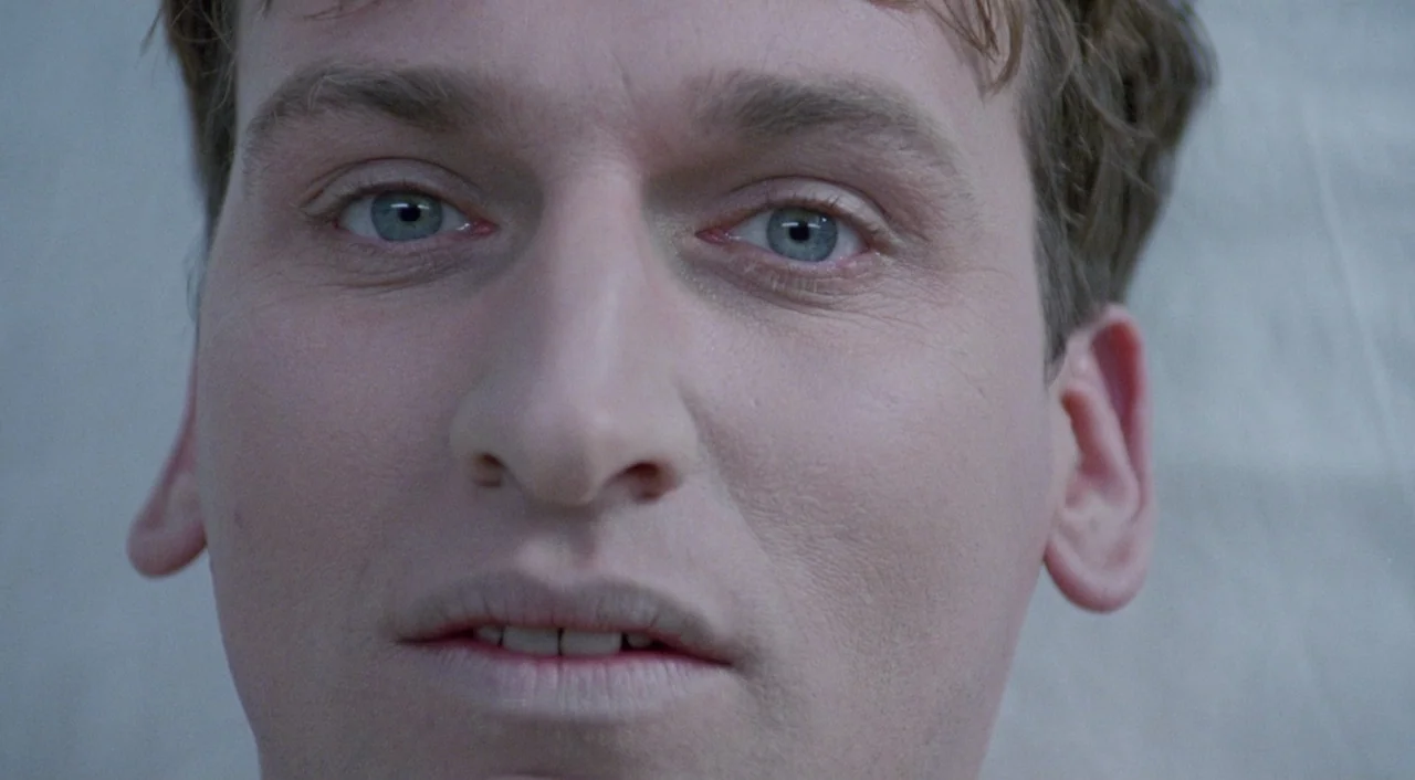Shallow Grave (1994) movie still: closeup — A man's face occupies the entirety of the frame against a plain light background. He gazes directly at…