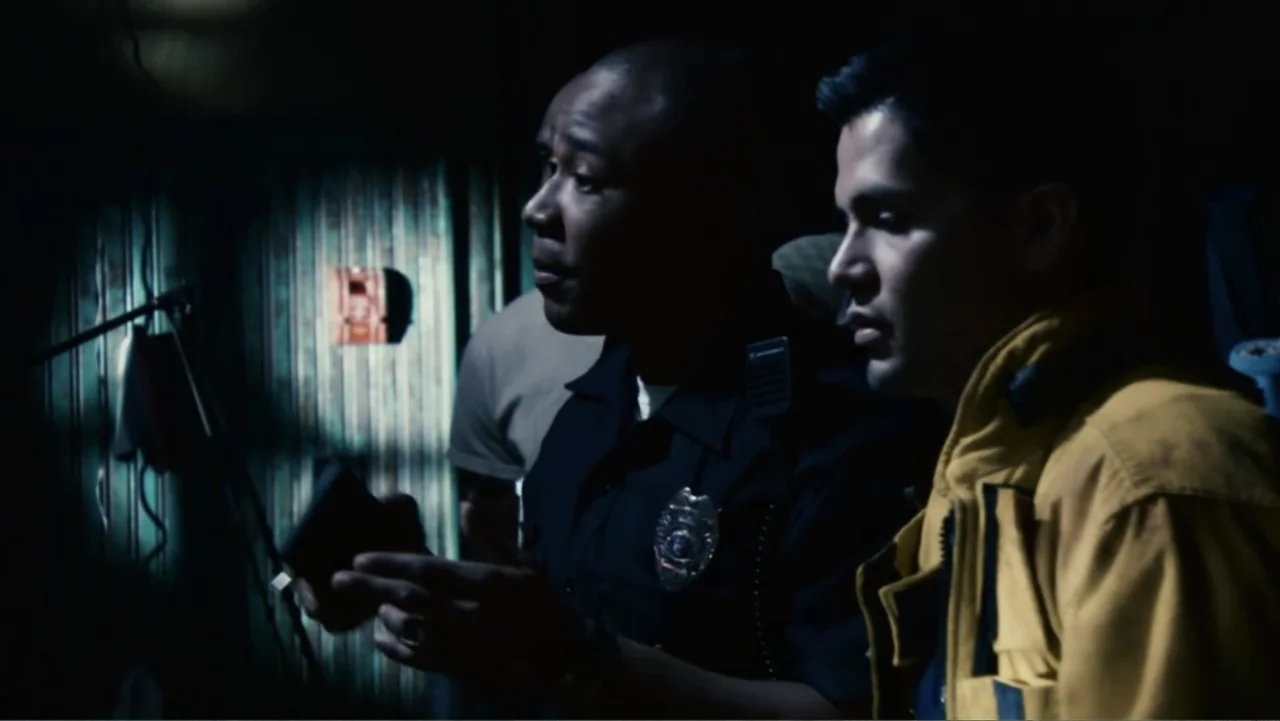 Quarantine (2008) movie still: medium — A dark indoor setting with vertical textured wall panels illuminated by a single harsh light. A uniformed…