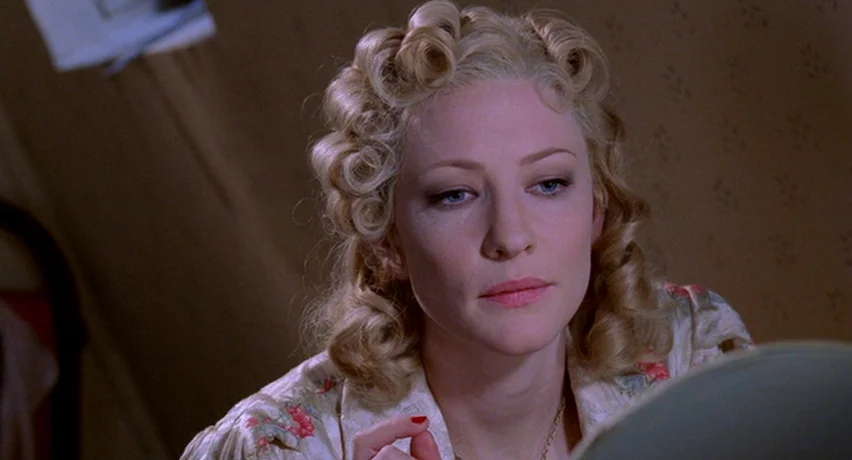 The Man Who Cried (2000) movie still: closeup — A woman sits before a mirror in a room with patterned beige wallpaper. She stares into her own…