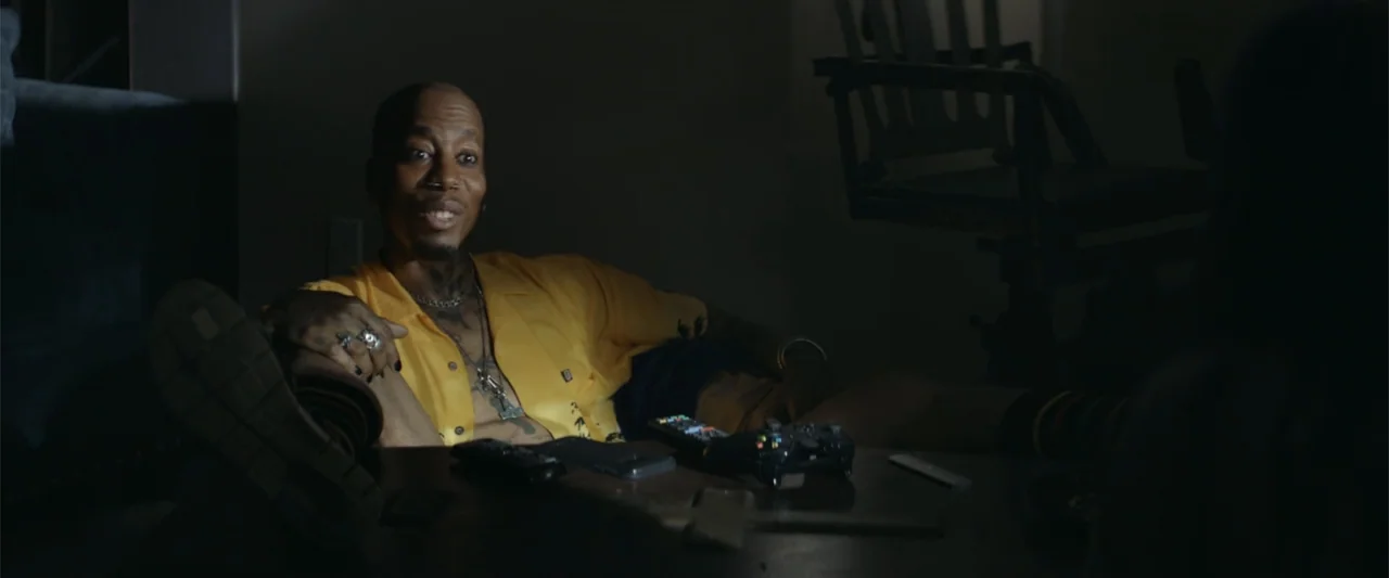 Mennonite's Bite (2023) movie still: medium — A dimly lit room at night features a man reclining on a sofa with his feet resting on a coffee table.…