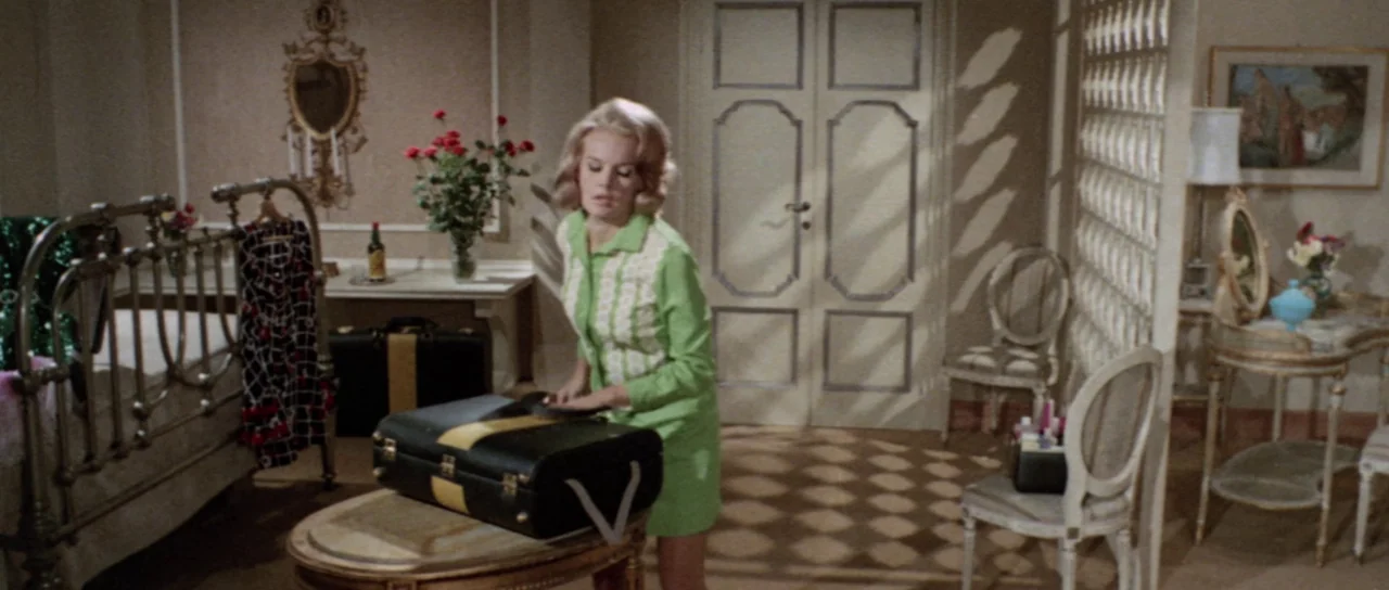Orgasmo (1969) movie still: medium — A 1960s hotel room features ornate furniture, patterned wallpaper, and a metal bed frame. A young blonde woman…