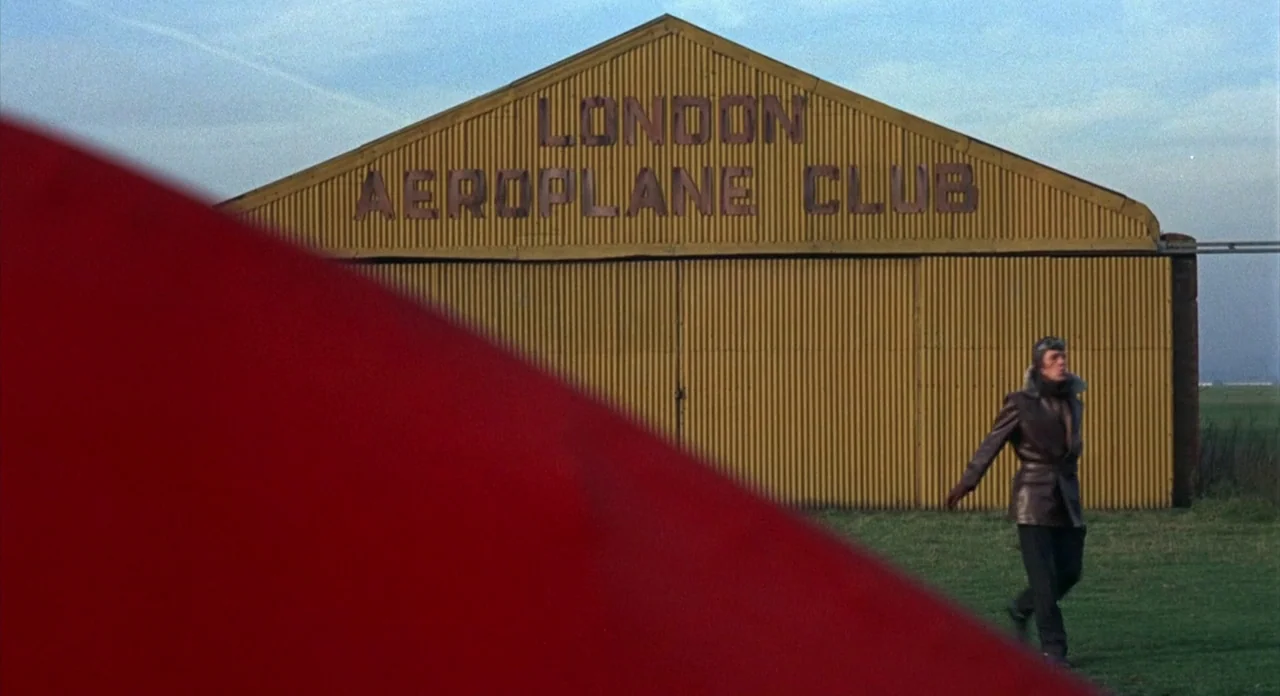 The Abominible Dr. Phibes (1972) movie still: wide — A yellow corrugated metal hangar building features large lettering identifying a London flying…