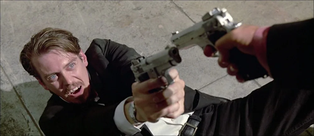 Reservoir Dogs (1992) movie still: medium — A flat concrete surface serves as the ground for a physical confrontation. A man in a suit lies on the…