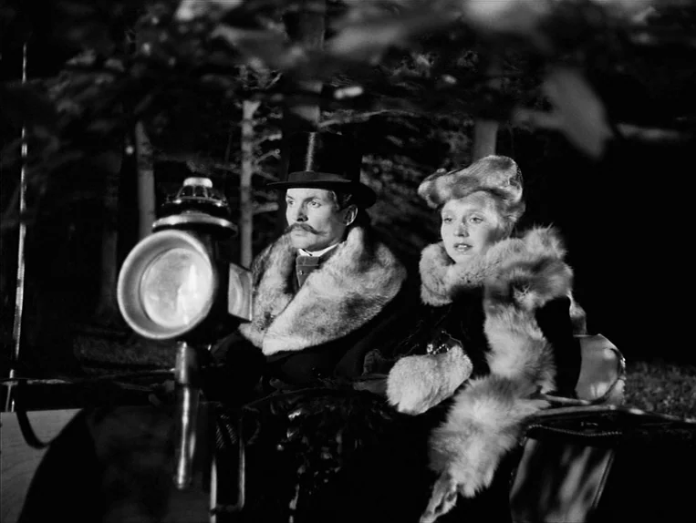 Effi Briest (1974) movie still: medium — A man and a woman sit together in an open horse-drawn carriage at night. They wear formal Edwardian era…