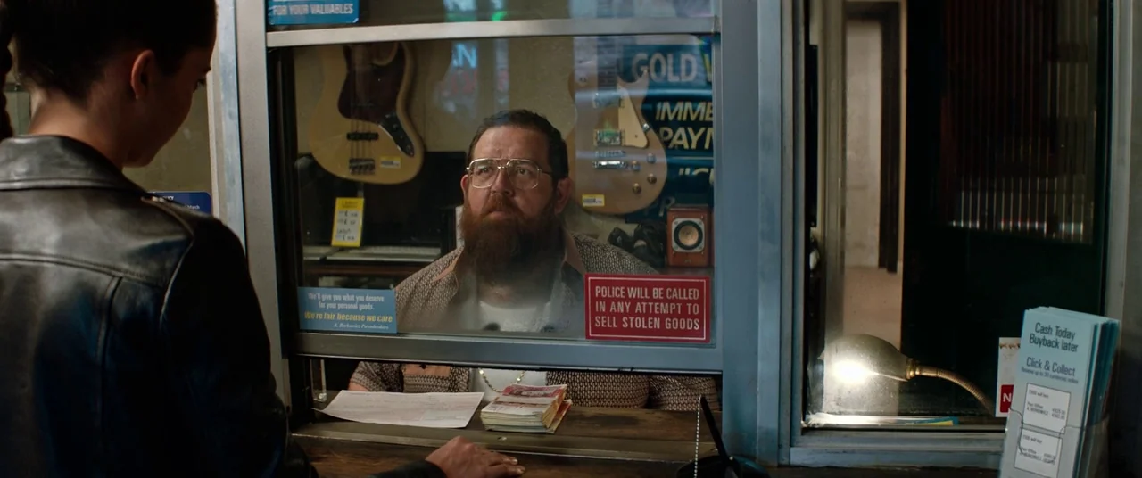 Tomb Raider (2018) movie still: medium — A man sits behind a secure plexiglass partition inside a pawn shop. He sits across from a woman at the…