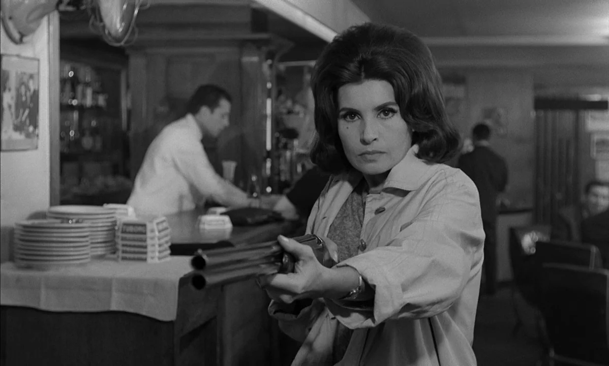 La Peau Douce (The Soft Skin) (1964) movie still: medium — A dimly lit bar interior features a wooden counter and stacked white plates. A woman with…