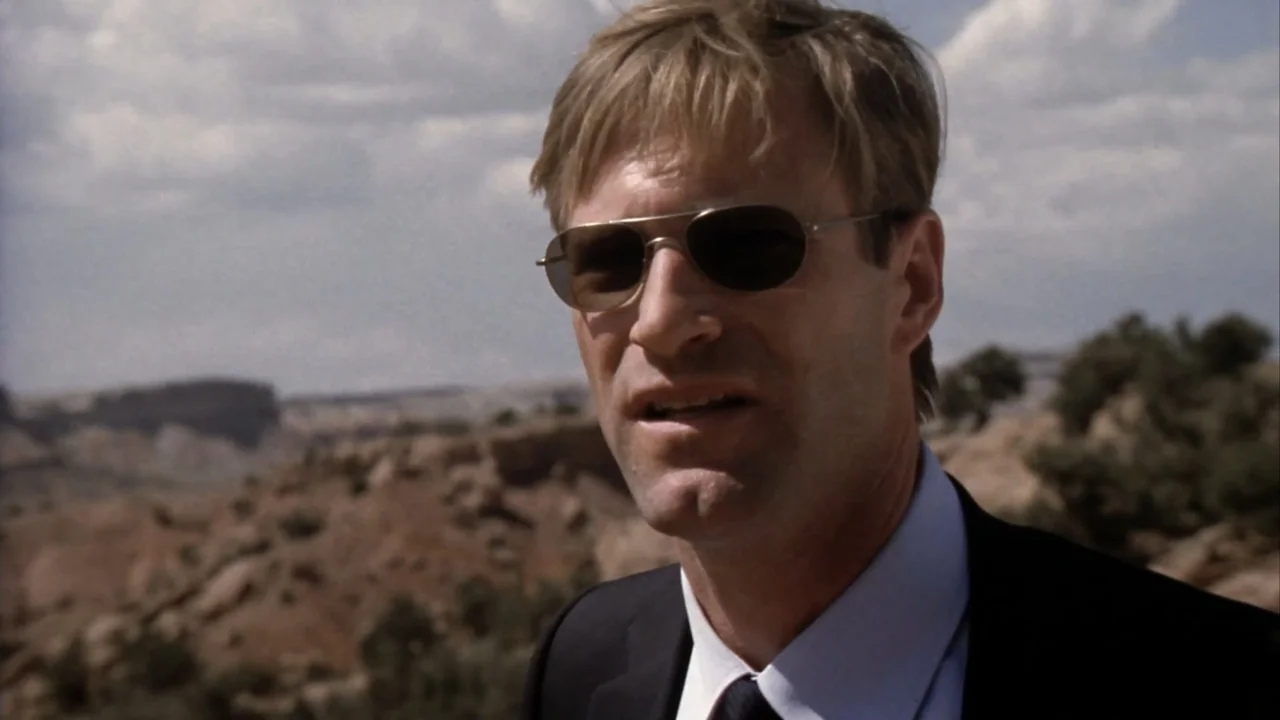 Suspect Zero (2004) movie still: closeup — A man in a suit stands in a sunlit desert landscape. The subject looks off-camera while wearing…