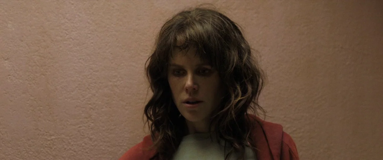 Destroyer (2018) movie still: closeup — A woman stands against a textured, solid beige wall in an indoor space. The woman looks downward while…