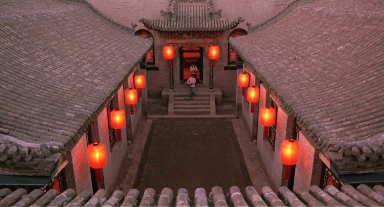 Raise The Red Lantern movie still: wide — A traditional Chinese courtyard features stone steps and gray tile roofs. A woman walks down the steps…
