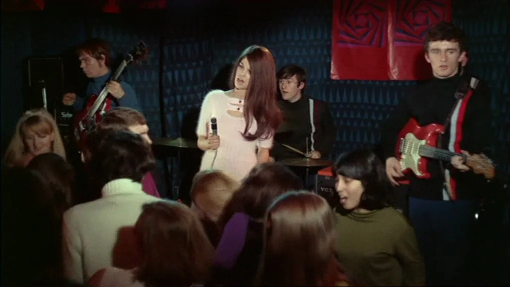The Sorcerers (1967) movie still: medium — A dimly lit club interior features a pop band performing for an audience. A woman in a light sweater…