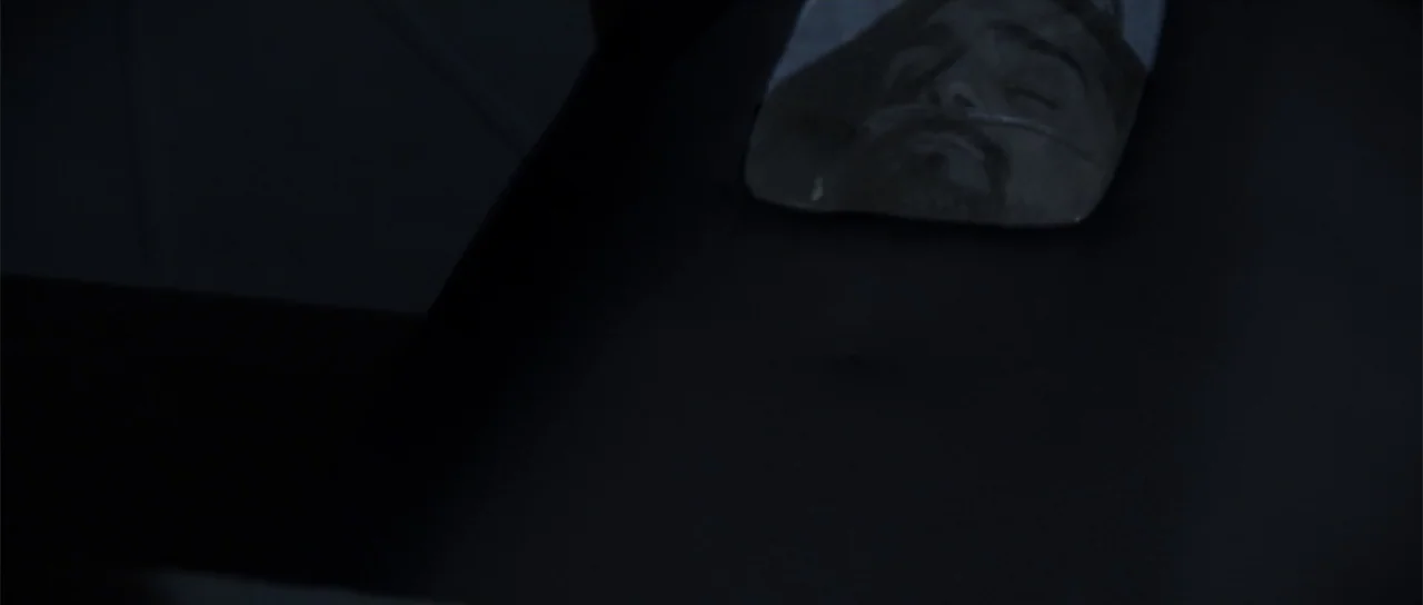 Astronaut: The Last Push (2012) movie still: closeup — A dark, nearly black bedroom space features a single reflective surface on a flat plane. A…