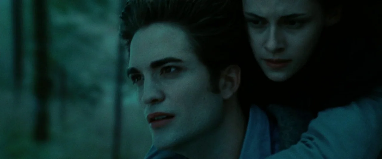 Twilight (2008) movie still: closeup — A man carries a woman on his back through a dark, hazy wooded area. They both look forward with serious…