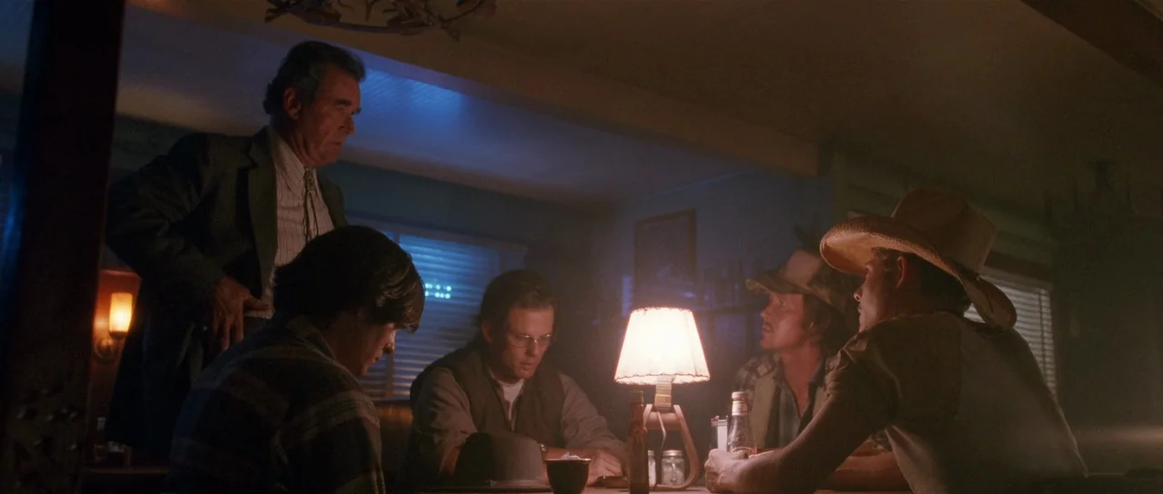 Fire In The Sky (1993) movie still: medium — A dimly lit diner booth features a group of five men sitting around a table. An old lamp illuminates…