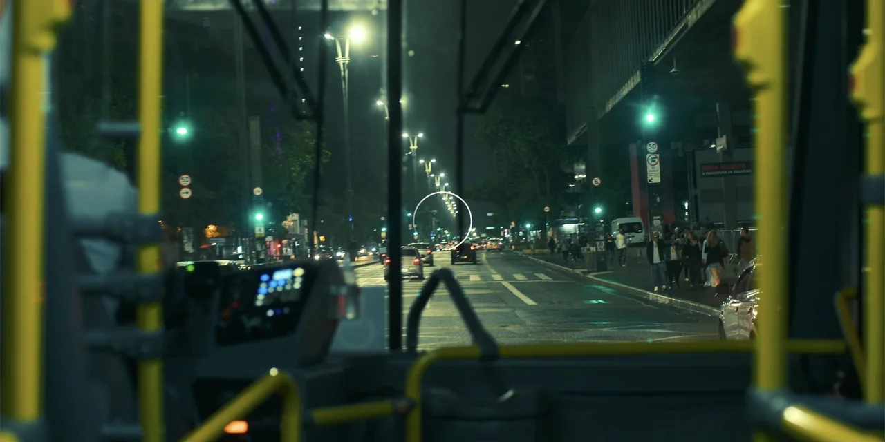 An Unforgettable Year - Autumn (2023) movie still: wide — A view through a bus windshield onto a dark city street at night. Vehicles and pedestrians…