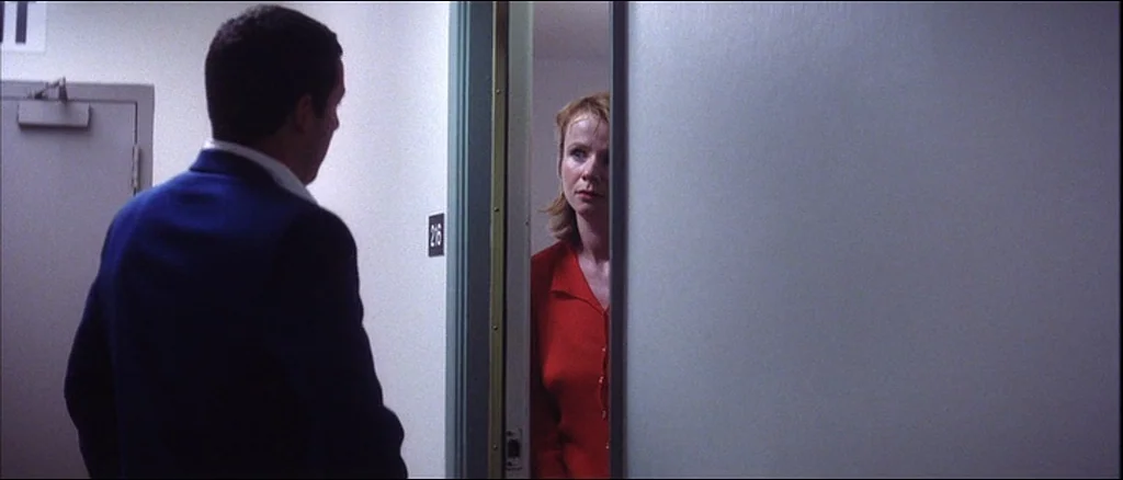 Punch Drunk Love (2002) movie still: medium — A utilitarian hotel corridor with beige walls and a numbered door. A man in a blue suit stands outside…