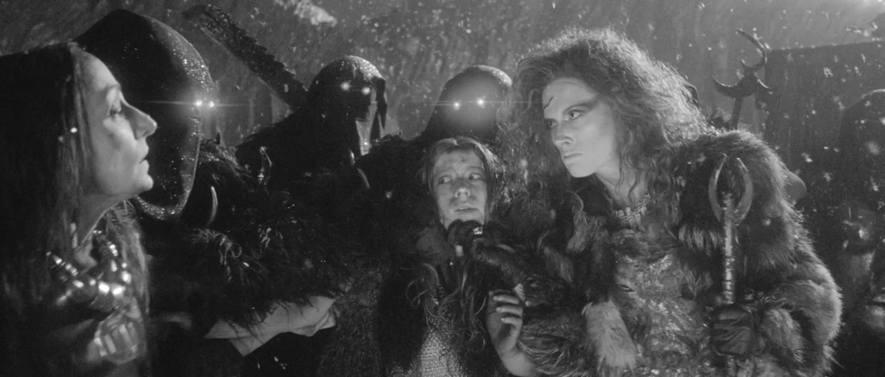 She Is Conann (2023) movie still: medium — A group of armored figures stands in a dark, snowy environment at night. A woman in fur armor holds a…