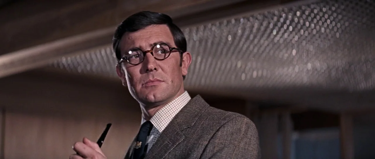 On Her Majesty’s Secret Service (1969) movie still: medium — An interior space features a wood-paneled wall and a prominent beaded light fixture. A…
