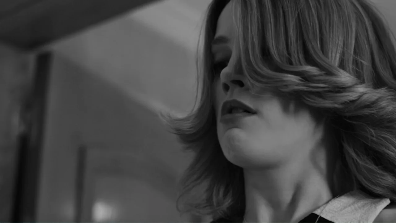 Creditors (2025) movie still: closeup — A close up view inside a bright room showing a woman looking down. She wears a sleeveless shirt while her…