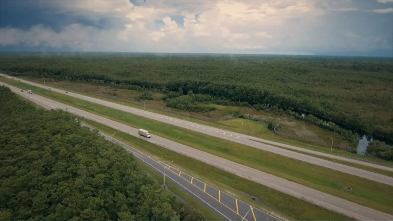 Aileen Wuornos : Mind of a Monster (2020) movie still: establishing — A vast multi-lane highway cuts through an expansive dense green forest…