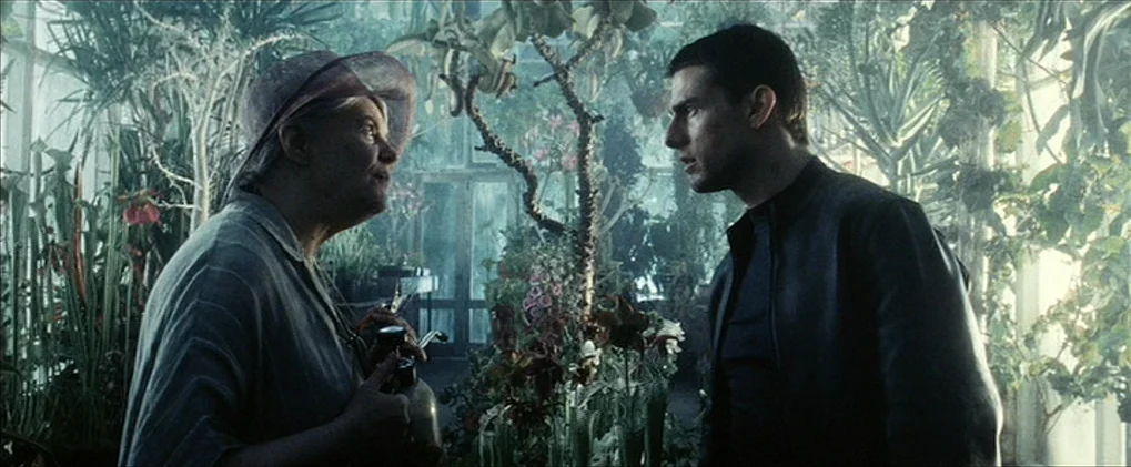 Minority Report movie still: medium — A dense interior space filled with potted tropical plants and glass paneling. An older woman and a man stand…