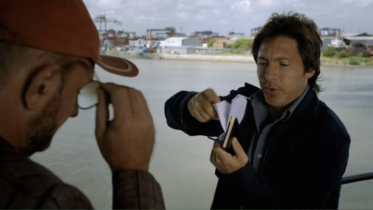 A Boyfriend for My Wife (2008) movie still: medium — A man stands on a waterfront pier with an industrial harbor in the background. He extracts a…