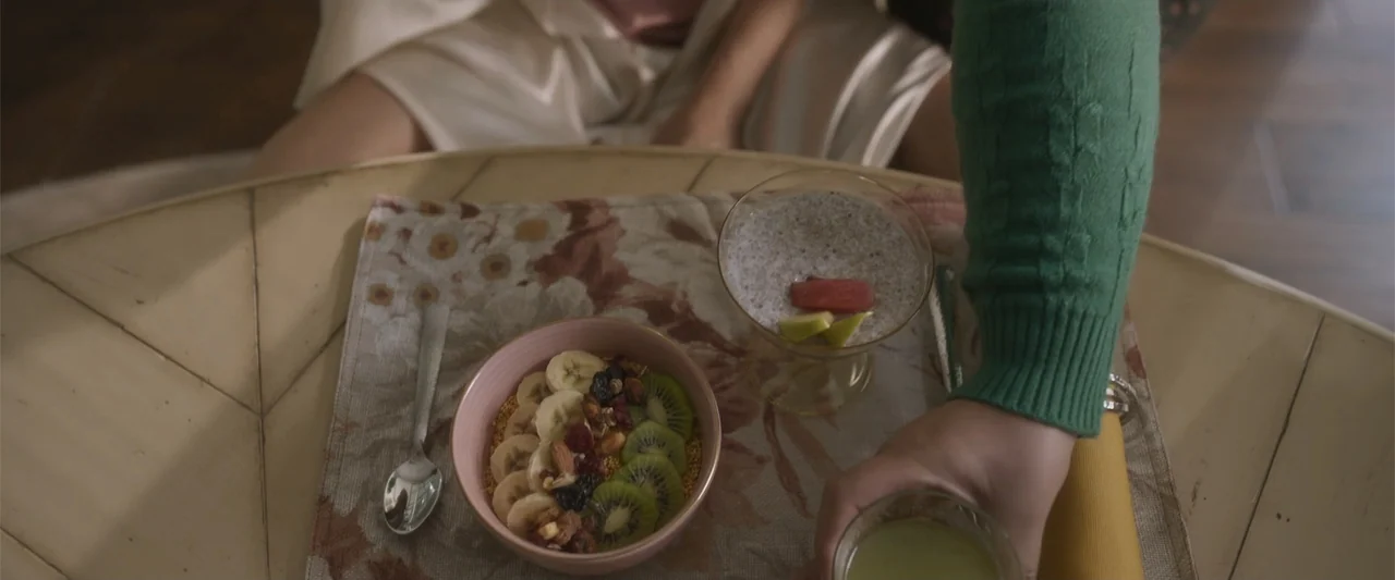 Crazy for Change (2020) movie still: medium — A breakfast tray sits on a table containing a bowl of fruit and chia pudding. A person in a green…