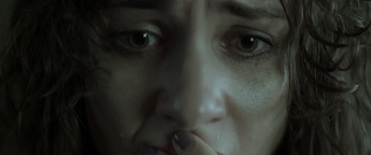 Lord of Misrule (2023) movie still: closeup — A close-up shot of a person's face inside a dark environment. The woman gazes directly at the camera…