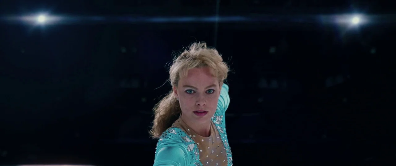 I, Tonya (2017) movie still: medium — A dark, empty ice rink is illuminated by intense overhead arena spotlights. A female ice skater in a sequined…