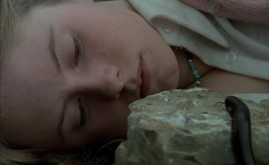 Black Moon (1975) movie still: closeup — A person lies on the ground in an outdoor environment with textured dirt. The subject's face is positioned…