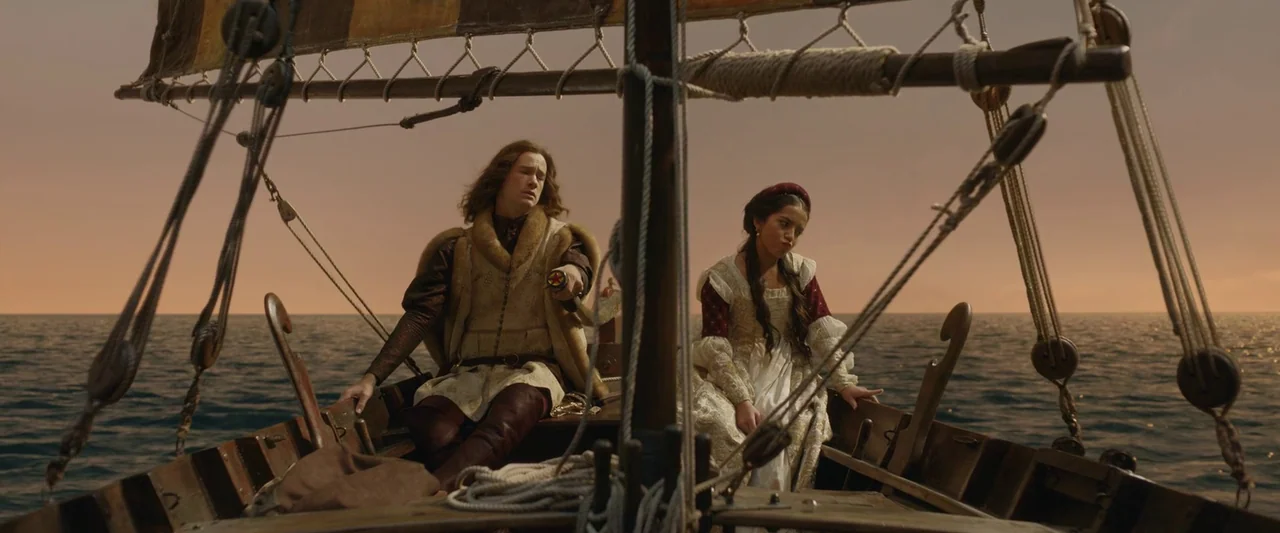 Rosaline (2022) movie still: medium — A wooden sailboat carries two people across a calm sea during golden hour light. The man gestures with his…
