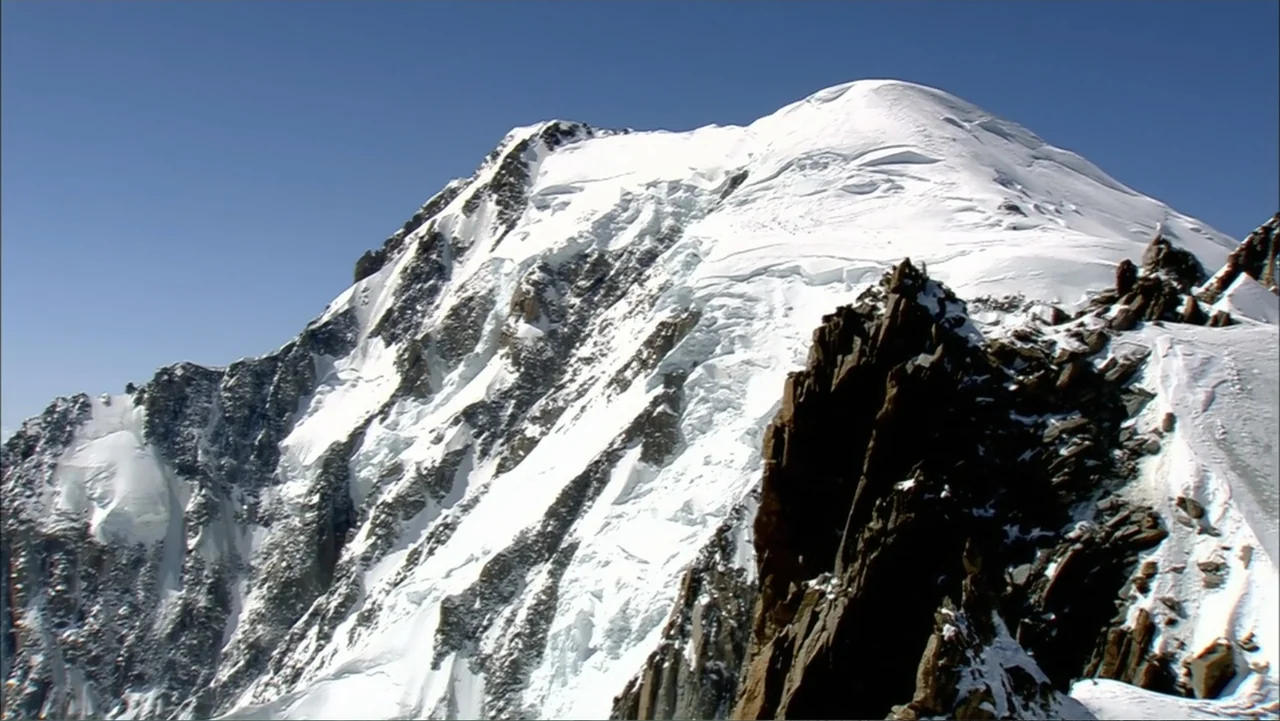 The Alps from Above: Symphony of Summits (2014) movie still: establishing — A high-altitude, snow-capped mountain peak stands against a clear, deep…