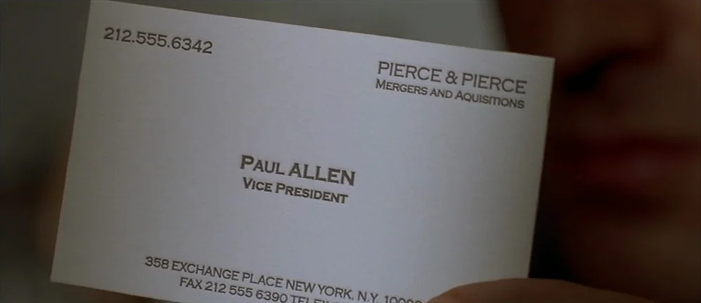 American Psycho (2000) movie still: closeup — A close-up shot focuses on a white business card held by a hand. The card features printed text…
