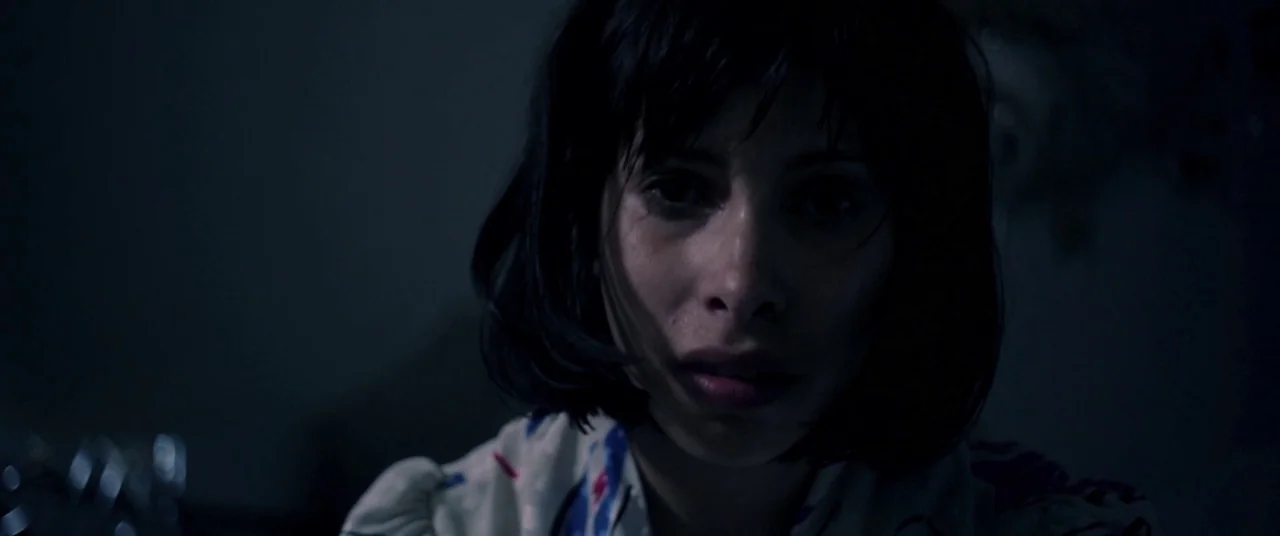 Here Comes The Devil (2012) movie still: closeup — A dark indoor space is dimly lit by a soft, directional light source. A woman with dark bobbed…