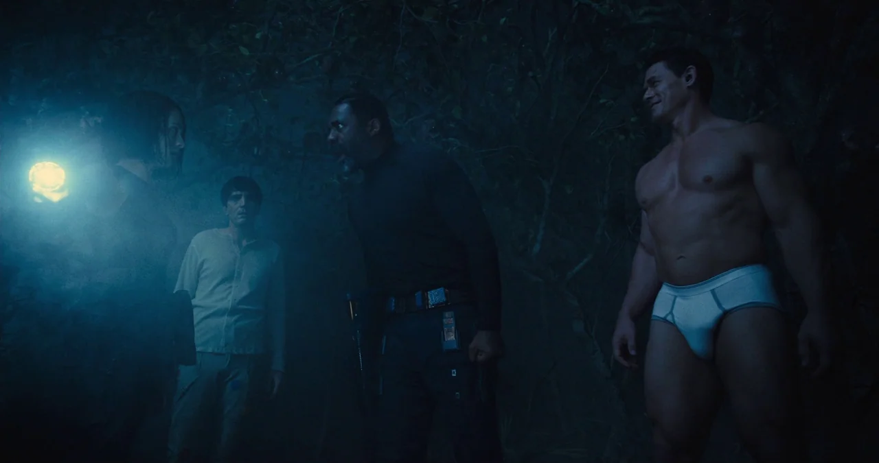 The Suicide Squad (2021) movie still: fullbody — A dark, dense jungle environment at night filled with heavy, overlapping tree branches. Four people…